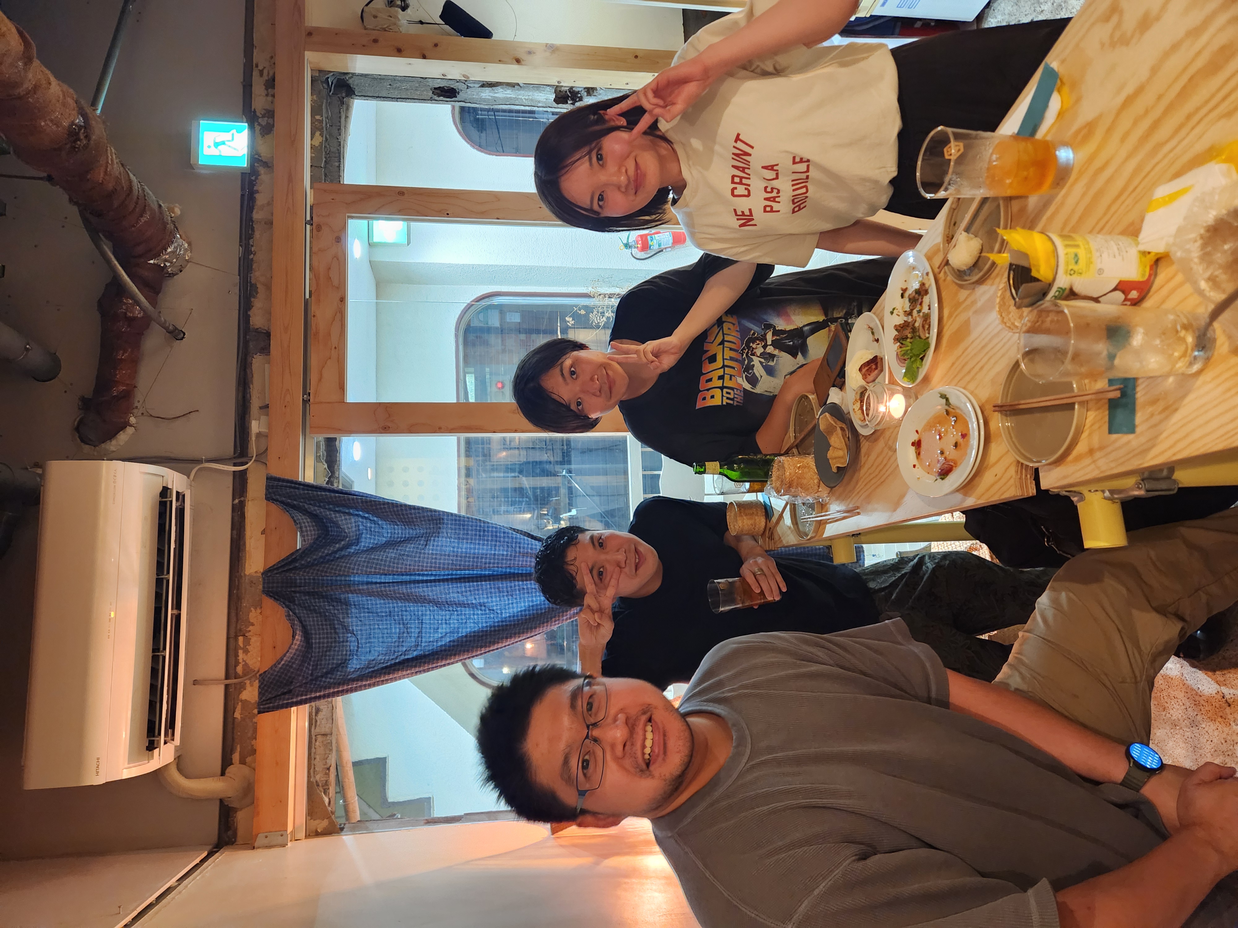 Four guests at the counter raising peace signs over Thai dishes and drinks