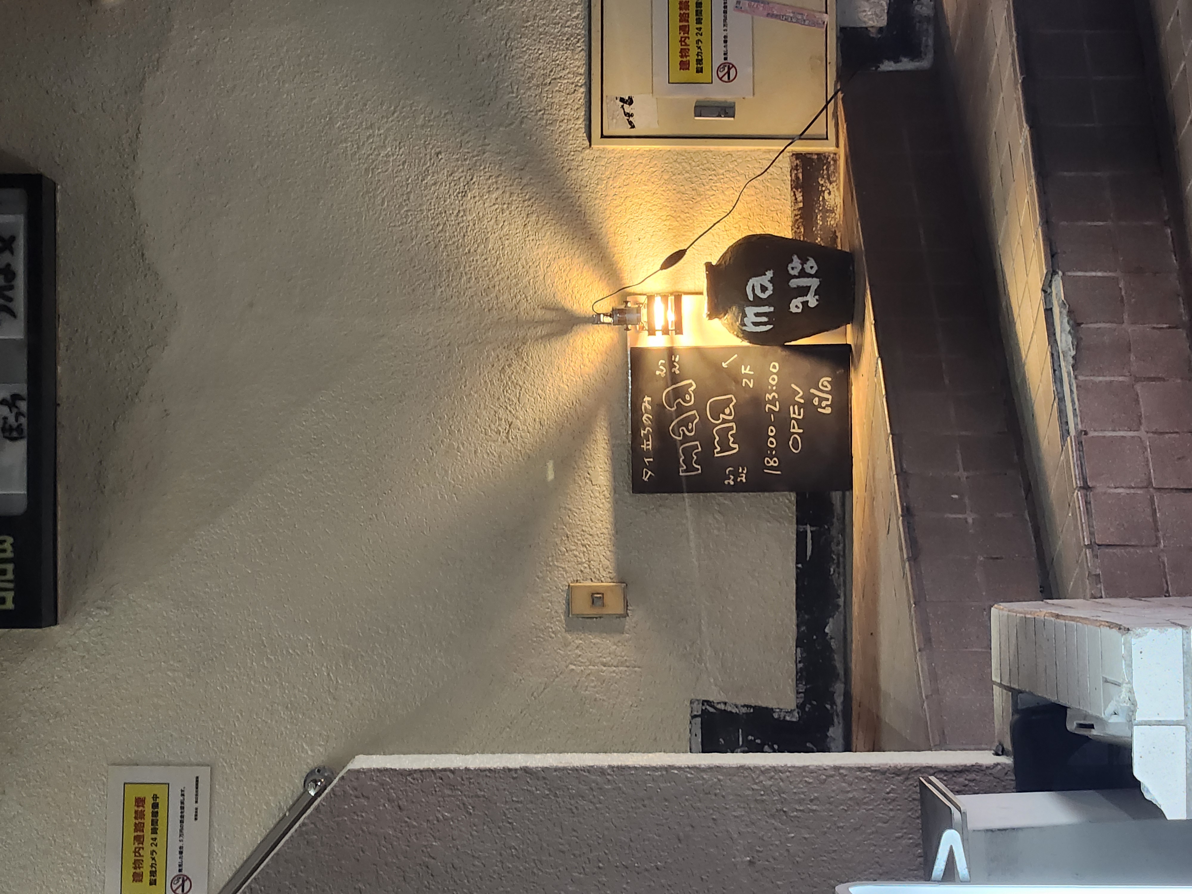 Hand-painted maama chalkboard sign lit by a warm sconce at the entrance